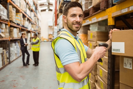 Warehouse worker scanning box while smiling at camera in a large warehouse